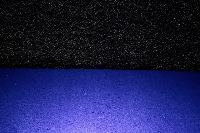 Fotografia w kształcie poziomego prostokąta. Zbliżenie na detal. Kadr podzielony poziomo na pół. Górna część to czarna tkanina haftowana koralikami. Dolna to niebieska tkanina.